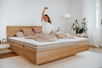 Eine Frau steht von einer SÁRA Spirit Doppelmatratze mit Morrison-Bezug auf. Die Maße der Matratze auf dem Foto betragen 180 x 200 x 22 cm.